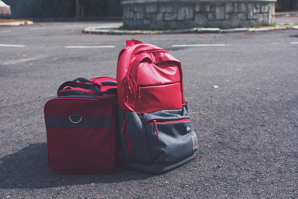 Red and grey coloured backpack and travel bag places on a road
