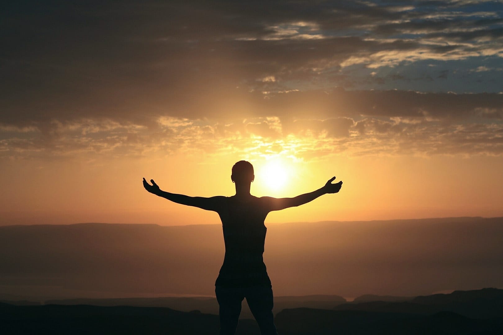 Person facing sunrise with open hands with their back facing us